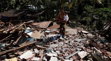 HABIS RANAP: Seorang lelaki mendukung anaknya ketika memeriksa rumahnya yang runtuh selepas gempa bumi melanda                          daerah Kayangan di Lombok Utara, Indonesia kelmarin. — Gambar Reuters