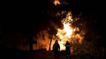 MARAK: Anggota bomba memantau kebakaran hutan berhampiran dengan kampung Psahna, di pulau Evia kelmarin. — Gambar Reuters 