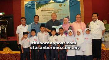 BANTUAN PENDIDIKAN: Awang Tengah (belakang tiga kiri) menyampaikan baucar bantuan persekolahan kepada murid  sebuah sekolah rendah di Lawas.