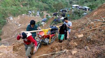 LALUAN BERBAHAYA: Penduduk membawa sebuah motosikal ketika mereka berjalan di sebatang jalan yang dihakis oleh tanah runtuh akibat Taufan Mangkhut di sebuah kem perlombongan kecil-kecilan di Itogon, Benguet, di Filipina, semalam. — Gambar Reuters