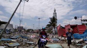 BENCANA ALAM: Penduduk tempatan membuat laluan di sepanjang jalan yang penuh dengan serpihan setelah gempa bumi dan tsunami melanda Palu di Pulau Sulawesi, semalam. — Gambar AFP