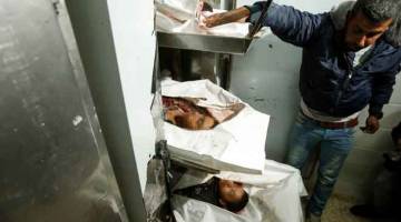 MATI SYAHID: Seorang lelaki melihat jenazah tiga rakyat Palestin yang terbunuh dalam serangan udara Israel di Semenanjung Gaza, di rumah mayat Hospital Al-Aqsa kelmarin. — Gambar AFP