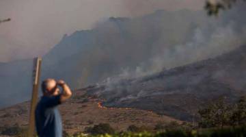 KEBAKARAN HUTAN TERBURUK: Orang melihat ke arah bukit yang terbakar dekat lebuh raya 101 Freeway di Thousands Oaks, California kelmarin. Pegawai California berkata kematian telah berlaku dalam kebakaran tersebut tetapi tidak menyatakan jumlah. Lebih 150,000 orang sudah dipindahkan. — Gambar AFP