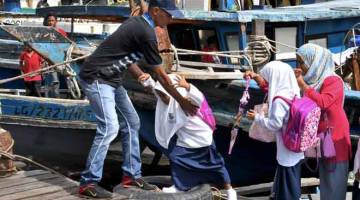 DEMI ILMU: Norshakinah dibantu oleh kru kapal penambang untuk turun dari kapal sebaik tiba di jeti bandar Sandakan untuk ke sekolah sambil ditemani ibunya Dayang Salmah (kanan) semalam. — Gambar Bernama