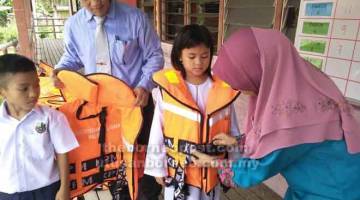 UTAMAKAN KESELAMATAN: Fatimah memakaikan jaket keselamatan kepada murid yang menaiki perahu semasa ke sekolah sambil dibantu oleh Nasrah.