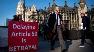 BANTAH PENANGGUHAN: Penunjuk perasaan pro-Brexit mempamerkan plakad kepda orang yang lalu di luar Dewan Parlimen di London pada 21 Februari lalu. — Gambar AFP