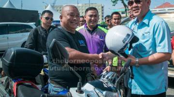 TINGKATKAN KEMPEN: Benny (kanan) menyampaikan topi keledar kepada seorang penunggang motosikal.