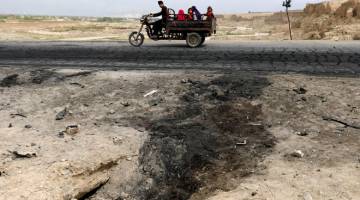 KESAN BOM: Sebuah keluarga Afghan melintasi tapak serangan bom kereta di mana tiga angota tentera AS maut dekat pangkalan udara Bagram, Afghanistan pada Selasa. — Gambar Reuters