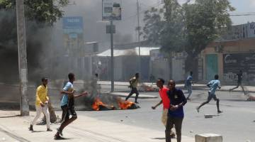 KECOH: Para penunjuk perasaan berlari melintasi tayar-tayar yang dibakar semasa protes antipolis di Somali yang membunuh seorang pemandu teksi beca dan penumpangnya di Mogadishu, kelmarin. — Gambar Reuters