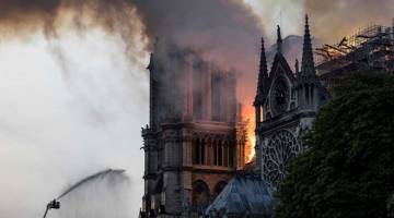 HANGUS: Anggota bomba memadamkan api yang berkepul-kepul dari bumbung Katedral Notre Dame di Paris pada Isnin. — Gambar AFP