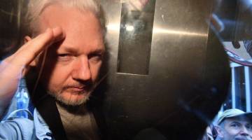 KE MAHKAMAH: Assange memberi tabik di sebalik kaca tingkap van penjara ketika dia dibawa ke Southwark Crown Court di London, Britain kelmarin. — Gambar AFP