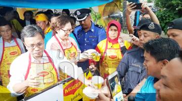 SHAFIE (kiri) dan Christina (dua kiri) mengagihkan bubur lambuk kepada orang ramai yang hadir di perkarangan bangunan DBKK.