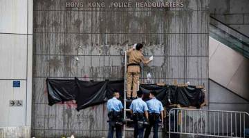DIKAWAL KETAT: Seorang pencuci mengikis tanda sementara anggota polis berdiri di depan grafiti yang ditutup pada dinding di luar ibu pejabat polis di Hong Kong, semalam. — Gambar AFP