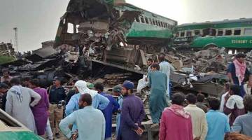 BERKECAI: Penduduk setempat berhimpun sekitar bangkai gerabak di tapak di mana dua kereta api berlanggar di daerah                         Rahim Yar Khan di wilayah Punjab, Pakistan kelmarin. — Gambar AFP