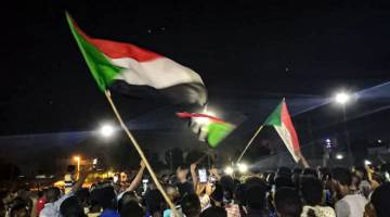 SUARA RAKYAT: Penunjuk perasaan mengayunkan bendera negara ketika berarak di jalan raya  di ibu negara Khartoum, Sudan, untuk menuntut pemerintahan awam kelmarin. — Gambar AFP