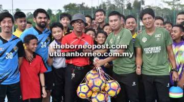 KLINIK BOLA SEPAK: Jurulatih Kuching FA, Mohd Sahrizan (dua kanan) menyerahkan bola kepada pihak sekolah pada sesi klinik bola sepak di Sekolah Menengah Sains Kuching.