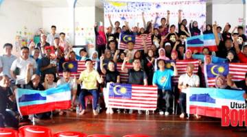 KIBAR: Frankie (depan, tengah) bersama penduduk Kampung Sim-Sim mengibarkan Jalur Gemilang dan bendera Sabah.