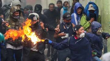 HURU-HARA: Penunjuk perasaan melontar bom minyak ke arah polis rusuhan ketika membantah pemansuhan subsidi bahan bakar di Quito, Ecuador kelmarin. — Gambar Ivan Alvarado/Reuters