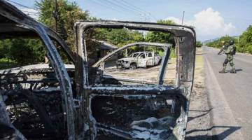 RENTUNG: Anggota tentera dilihat berkawal dekat kenderaan polis yang musnah dibakar dalam serangan hendap oleh sekumpulan lelaki bersenjata di Michoacan, Mexico kelmarin. — Gambar Enrique Castro/AFP