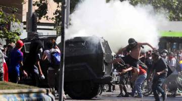 GANAS: Penunjuk perasaan menendang kenderaan berperisai semasa bantahan terhadap model ekonomi negeri Chile di Santiago, Chile kelmarin. — Gambar Ivan Alvarado/Reuters