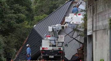 ROBOH: Anggota penyelamat menggeledah rumah yang roboh dalam kejadian tanah runtuh akibat hujan lebat di bandar Sakura, wilayah Chiba, Jepun semalam. — Gambar Jiji Press/AFP
