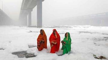 JEREBU TEBAL: Wanita Hindu memuja Dewa Matahari sambil berendam di dalam air tercemar Sungai Yamuna semasa festival Chatth Puja di New Delhi, kelmarin. — Gambar Reuters