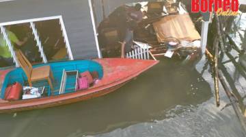 BANTUAN: Penduduk kampung menggunakan perahu mengangkut barang-barang mangsa yang masih boleh digunakan.