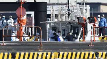HATI-HATI: Pekerja perubatan memakai sut pelindung dilihat mengiringi penumpang yang didapati positif bagi Koronavirus              dari kapal persiaran Diamond Princess di pangkalan Pengawal Pantai Jepun di Yokohama semalam. — Gambar AFP