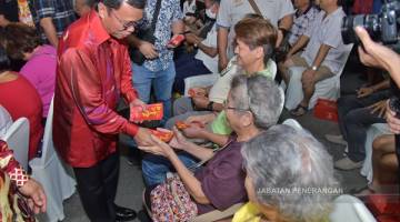 ANG PAO: Shafie (berdiri, tengah) menyampaikan 'ang pao' kepada 220 warga emas semasa majlis tersebut.