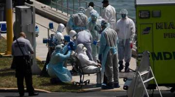 BANTU: Pekerja perubatan membantu anggota kru kapal persiaran disyaki dijangkiti COVID-19 yang tiba di Pangkalan Pengawal Pantai Amerika Syarikat di Miami, Florida kelmarin. — Gambar AFP