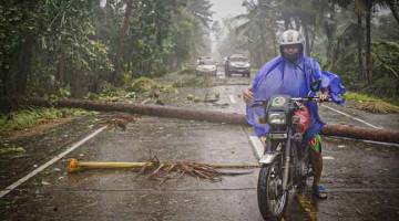 BERBAHAYA: Penunggang motosikal menempuhi hujan dan angin kencang di lebuh raya yang dipenuhi serpihan pokok kelapa yang tumbang di bandar Can-avid, wilayah Samar Timur kelmarin selepas Taufan Vongfong melanda. — Gambar AFP