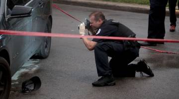CARI PETUNJUK: Anggota polis mengambil gambar lubang peluru pada pintu sebuah kereta selepas insiden tembakan di satu upacara pengebumian di Chicago, Illinois kelmarin. — Gambar AFP