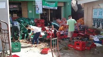 BERSELERAK: Gambar diambil daripada rakaman video amatur menunjukkan beberapa pekerja kedai mengemas botol-botol yang berselerak selepas gempa bumi melanda berhampiran bandar Cataingan, Masbate semalam. — Gambar AFP