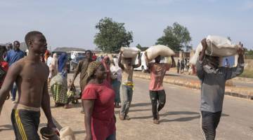 PENUHI STOK: Orang ramai membawa balik barang makanan dari sebuah gudang makanan yang digeledah di Jos, Nigeria. — Gambar AFP