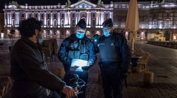 TEGAS: Anggota polis persekutuan CRS menyoal siasat seorang penunggang basikal ketika menjalankan rondaan di Place du Capitol, Toulouse, barat daya Perancis Sabtu lalu pada permulaan perintah berkurung bagi mengekang penularan COVID-19. — Gambar AFP