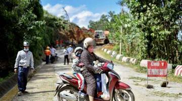 JALAN TUTUP: Seorang wanita yang menunggang skuter bersama anaknya terpaksa berpatah balik selepas tanah runtuh menimbus jalan raya ekoran hujan lebat yang dibawa oleh Taufan Molave di wilayah Quang Nam di tengah Vietnam semalam. — Gambar AFP