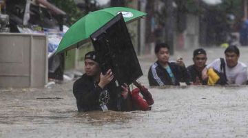 BANJIR TERUK: Seorang lelaki kelihatan mengangkat peti televisyen ketika dia dan penduduk yang lain mengharungi jalan dilanda banjir selepas Taufan Vamco melanda Bandar Marikina         di Manila kelmarin. — Gambar AFP