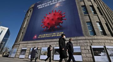 GELOMBANG KETIGA: Orang ramai melintas di hadapan bangunan majlis bandar raya yang memaparkan poster menggambarkan COVID-19 sebagai bom untuk memberi amaran mengenai penularan koronavirus baharu itu di Seoul, baru-baru ini. — Gambar AFP
