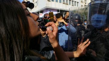 SIMBOLIK: Seorang wanita mencalit gincu pada bibirnya semasa berdepan barisan pegawai polis yang membentuk perisai manusia bagi menyekat akses penunjuk perasaan ke pusat bandar di Tunis, kelmarin. — Gambar AFP