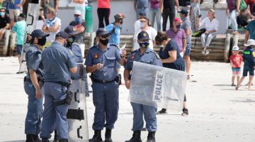 TUGAS SUKAR: Anggota polis berseragam antirusuhan lengkap dengan perisai meronda semasa tunjuk perasaan di pantai Muizenberg di Cape Town, kelmarin. — Gambar AFP