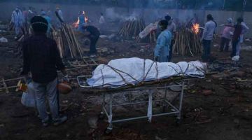 KORBAN COVID-19: Ahli keluarga (kiri) kelihatan menunggu giliran di sebelah mayat korban COVID-19 di kawasan pembakaran mayat di New Delhi, kelmarin. — Gambar AFP