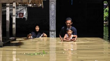 BANJIR TERUK: Seorang lelaki bersama keluarganya mengharungi air banjir yang mencecah paras dada di luar sebuah rumah di kawasan Gampong Meunasah di Aceh Utara, kelmarin. — Gambar AFP