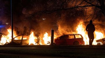 Seorang penunjuk perasaan berdiri tidak jauh dari kereta yang terbakar di Malmo selepas rusuhan membantah provokasi membakar naskhah al-Quran semakin tegang. — Gambar AFP