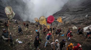 Penduduk kampung menggunakan jaring untuk menangkap persembahan yang dicampak oleh suku Tengger ketika upacara keagamaan Hindu di kawah gunung berapi Bromo yang aktif di Probolinggo, wilayah Jawa Timur kelmarin. — Gambar AFP