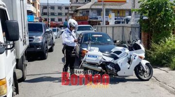 PERIKSA: Anggota trafik memeriksa kereta yang parkir di bahu jalan.