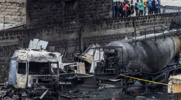 Orang ramai berdiri di atas dinding bangunan yang rosak untuk melihat rangka trak yang hangus, sehari selepas kebakaran besar akibat letupan memusnahkan kawasan Embakasi di Nairobi pada Khamis lepas. — Gambar AFP