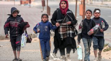 Seorang wanita berjalan kaki bersama anak-anaknya selepas melarikan diri daripada pengeboman di kawasan hospital Al-Shifa ketika mereka tiba di kem pelarian Nuseirat di tengah Semenanjung Gaza kelmarin. — Gambar AFP