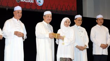 SERAH: Hajiji menyampaikan sumbangan duit raya kepada salah seorang wakil pelajar sempena di majlis itu.