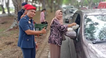 Wan Kamarudin (kiri) dan beberapa pihak menyampaikan bubur lambuk kepada pengguna jalan raya di Bintulu, petang Selasa.