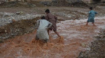 Kanak-kanak dilihat mengharungi banjir berhampiran jalan raya yang rosak selepas hujan lebat di pinggir bandar Quetta kelmarin. — Gambar AFP